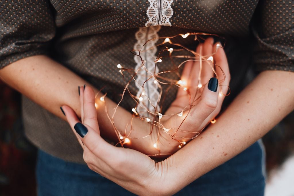 Close-up of a woman's hands gently holding glowing string lights, creating a warm festive vibe.